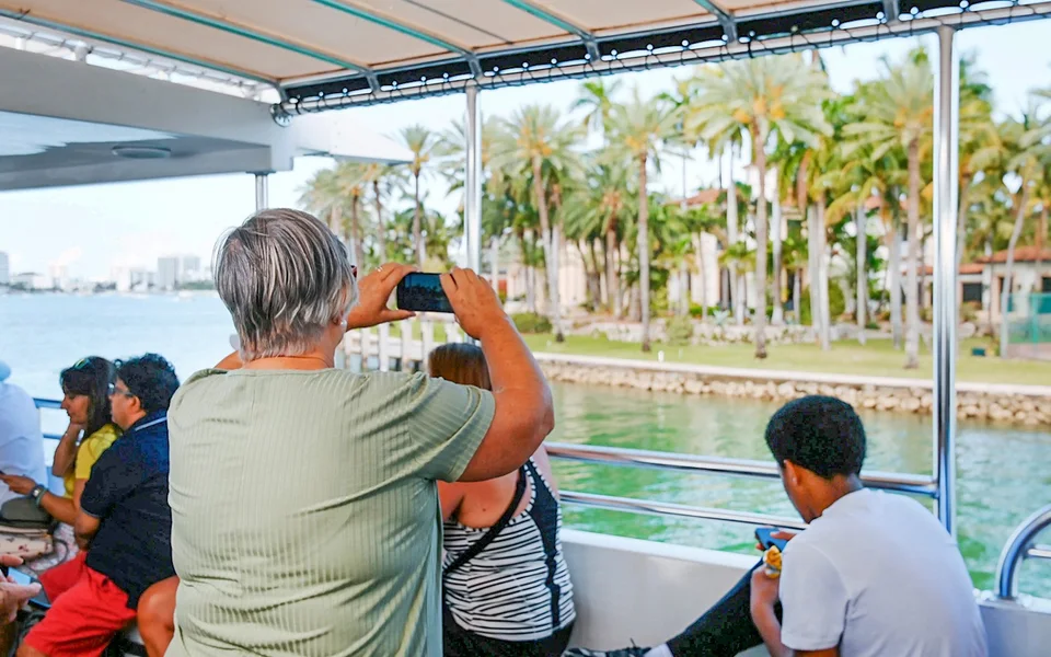 Passenger photographing palm-lined waterfront from a boat